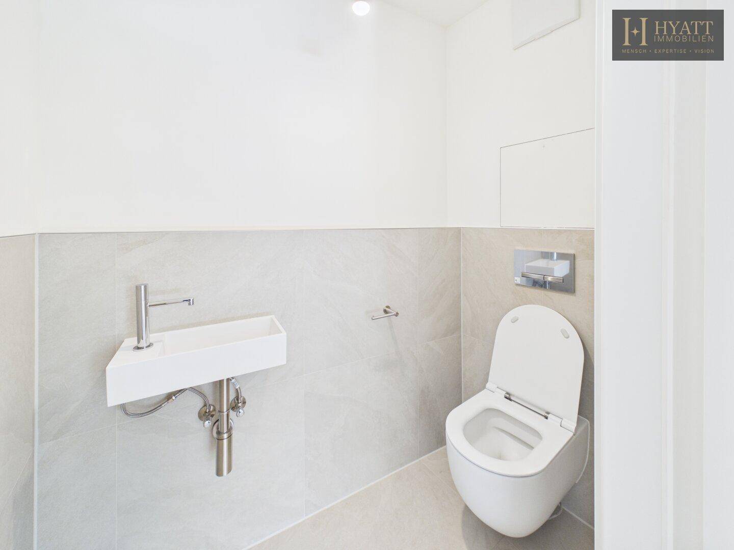 Modernes Gäste-WC mit wandhängender Toilette und kleinem Handwaschbecken.