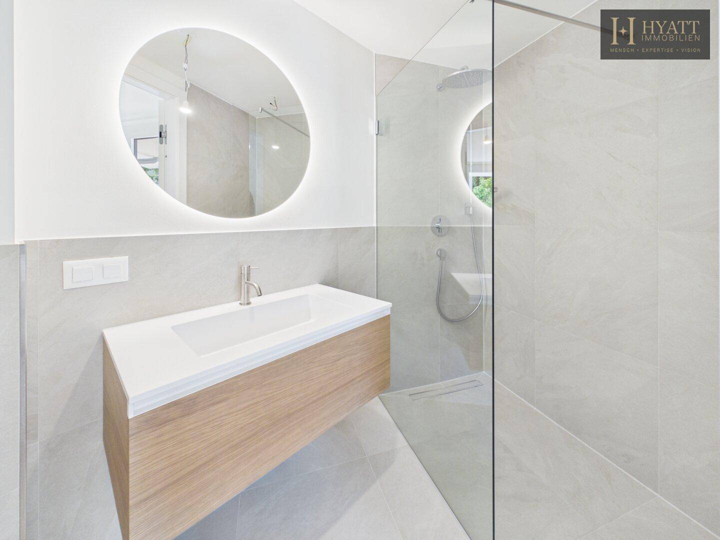 Modernes Badezimmer mit begehbarer Dusche, schwebendem Waschtisch und beleuchtetem Spiegel.