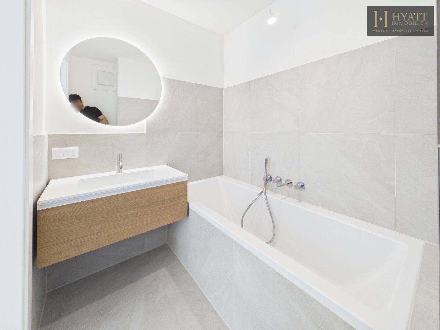 Zeitgemäßes Badezimmer mit Badewanne, Waschtisch und großformatigen Fliesen.