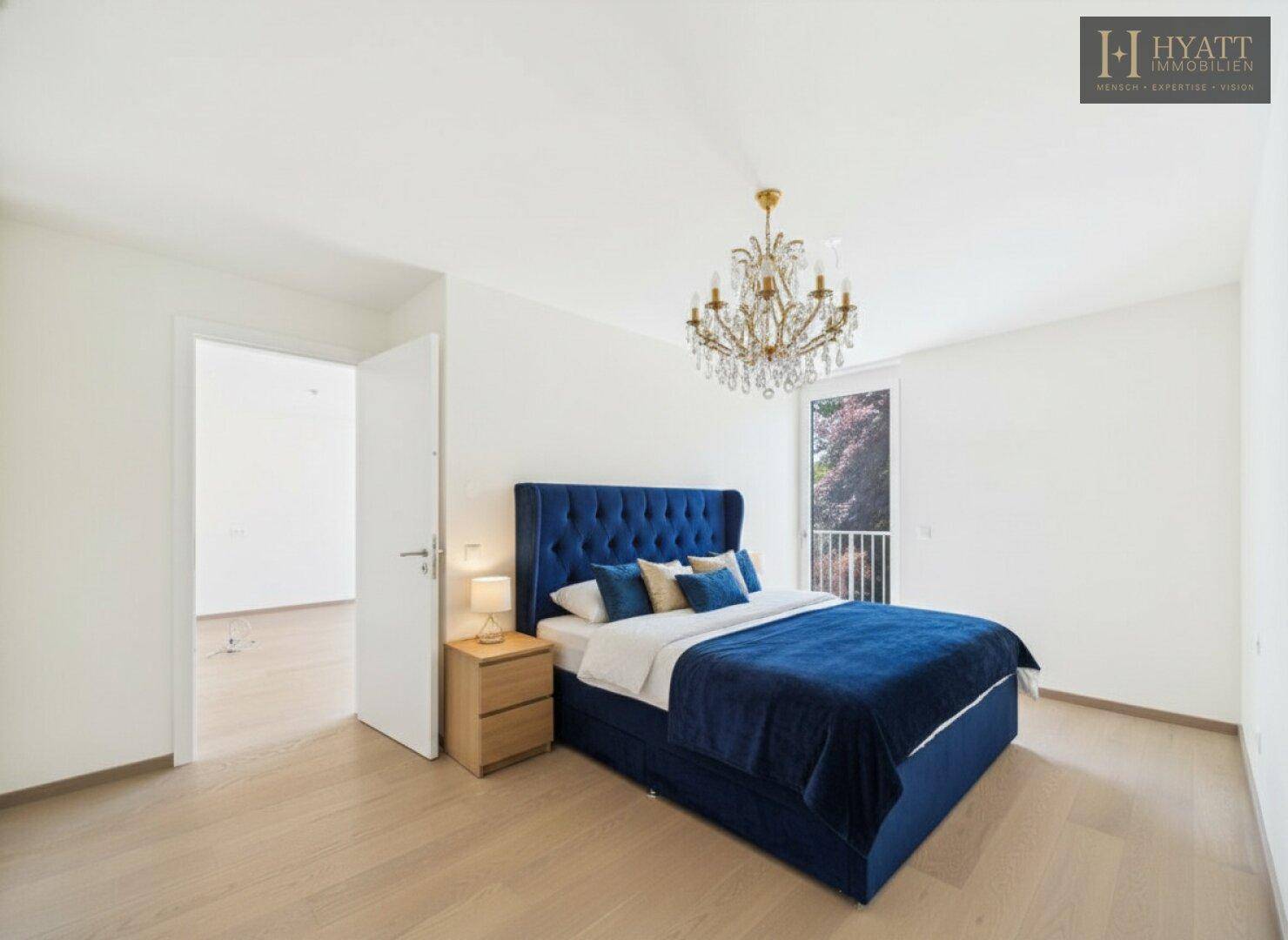 Elegantes Schlafzimmer mit blauem Bett, Kronleuchter und Balkonzugang.
