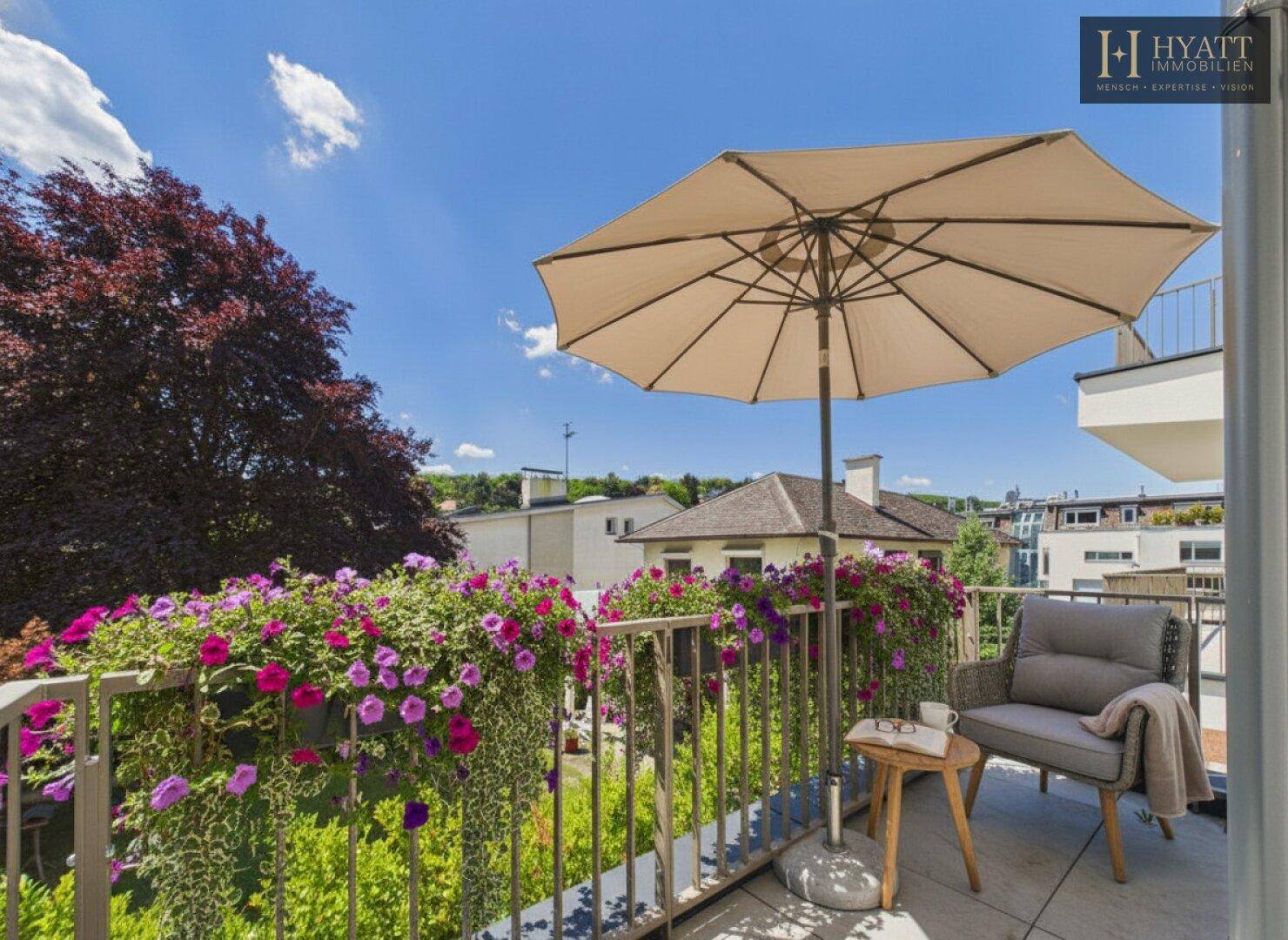 Möblierter Balkon mit Sonnenschirm, Blumenkästen und Blick ins Grüne.