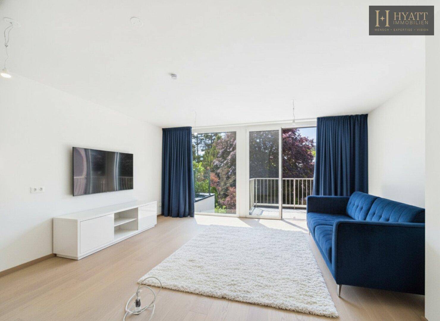 Gemütliches Wohnzimmer mit blauem Sofa, großem Fenster und Zugang zum Balkon.