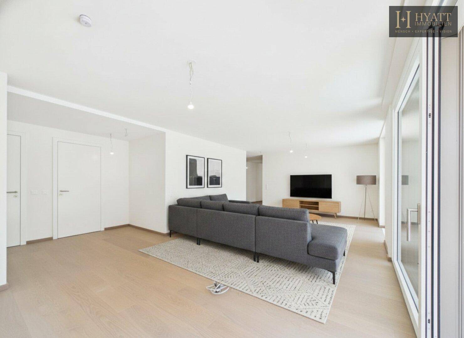 Modern eingerichtetes Wohnzimmer mit großem Sofa und viel Tageslicht durch die Fensterfront.