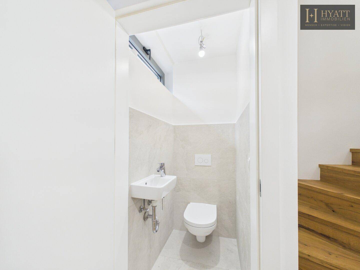 Modernes Gäste-WC mit Wand-WC und kleinem Waschbecken, hell gefliest.