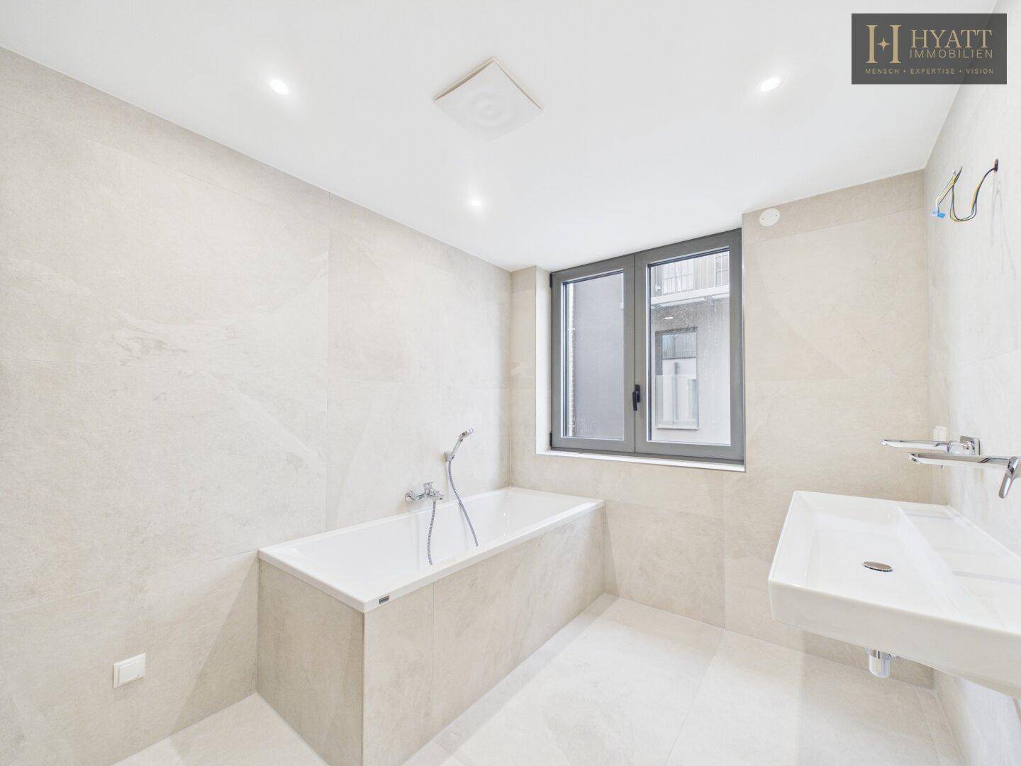 Modernes Badezimmer mit Badewanne und Einzelwaschbecken, komplett gefliest in hellen Farbtönen.