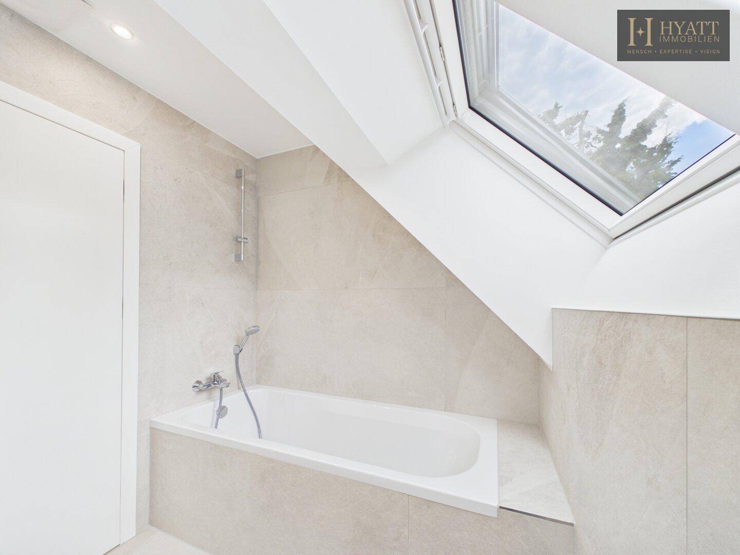 Modernes Badezimmer im Dachgeschoss mit Badewanne und Dachfenster, das viel Licht spendet.