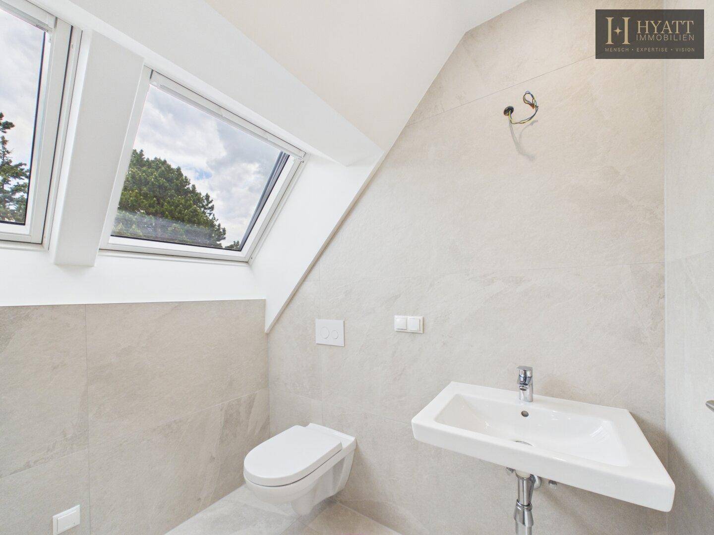 Helles Badezimmer im Dachgeschoss mit WC, Waschbecken und zwei Dachfenstern.