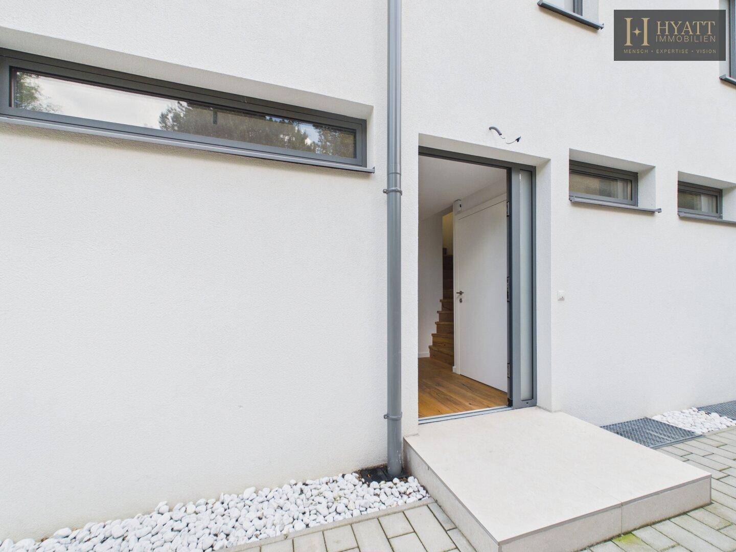 Eingangsbereich des Hauses mit moderner Tür und kleiner Rampe für barrierefreien Zugang.