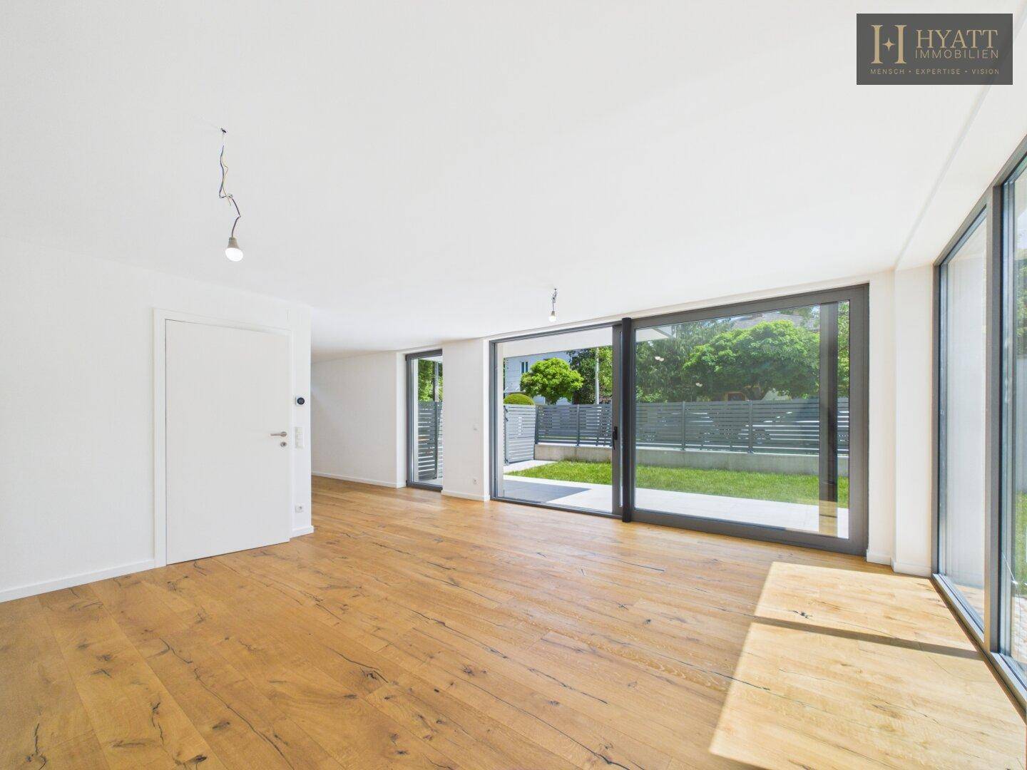 Helles Wohnzimmer mit großen Fensterfronten, Holzboden und Zugang zum Garten.