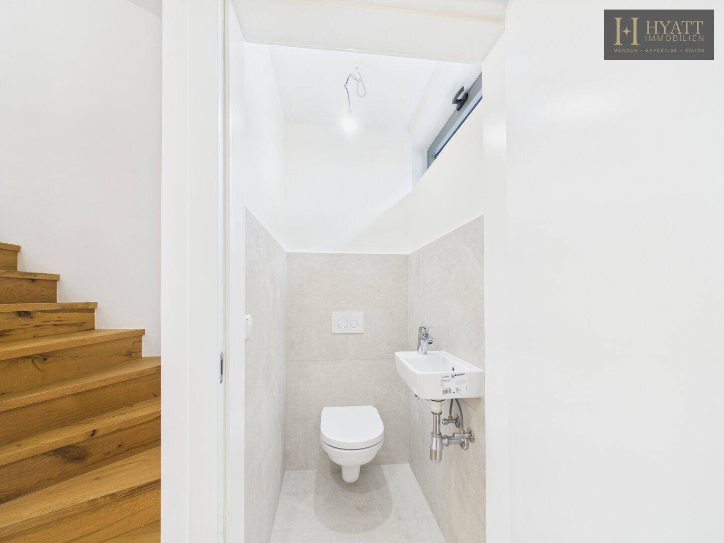 Modernes Gäste-WC mit Wand-WC, kleinem Waschbecken und hellen Fliesen.