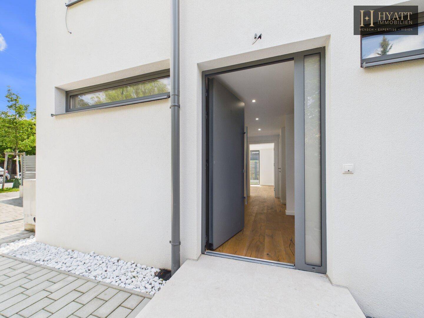 Eingangsbereich des modernen Hauses mit breiter Tür und gepflastertem Vorplatz.
