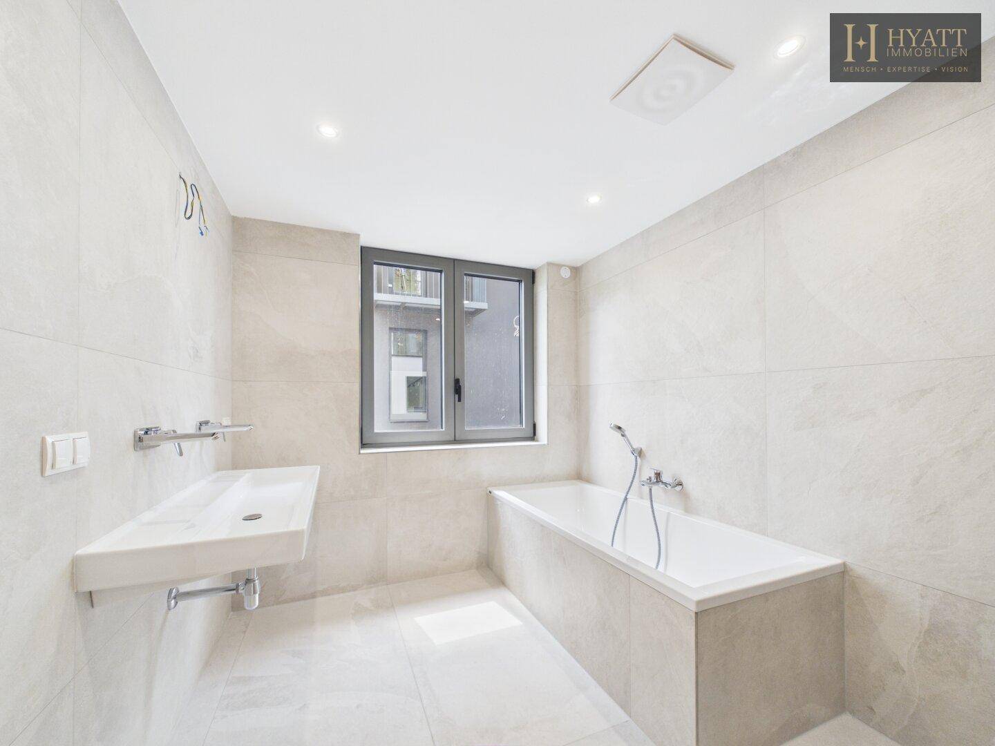 Modernes Badezimmer mit Badewanne, elegantem Waschbecken und großen hellen Fliesen.