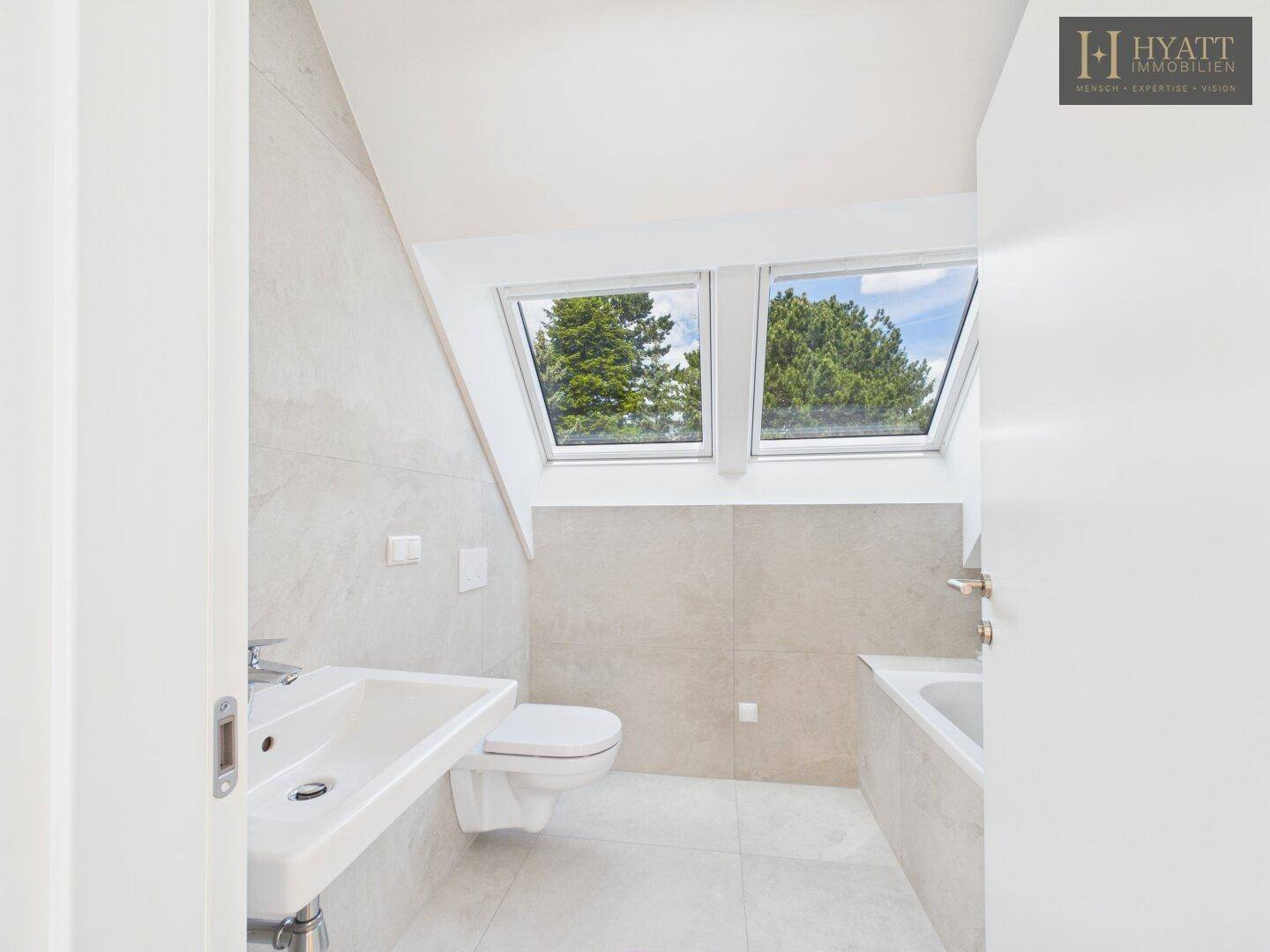Helles Dachgeschoss-Badezimmer mit Badewanne, WC, Waschbecken und zwei Dachfenstern.