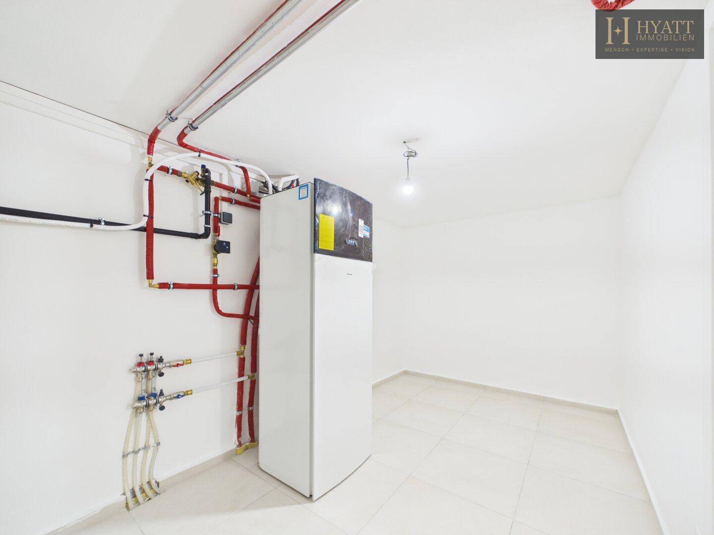 Technikraum im Keller mit Heizungsanlage und sichtbaren Installationen.