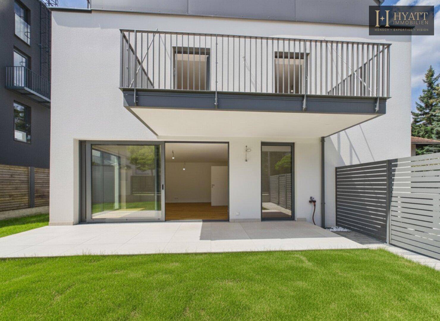 Rückansicht des Hauses mit großzügiger Terrasse, Rasenfläche und Zugang zum Innenbereich.