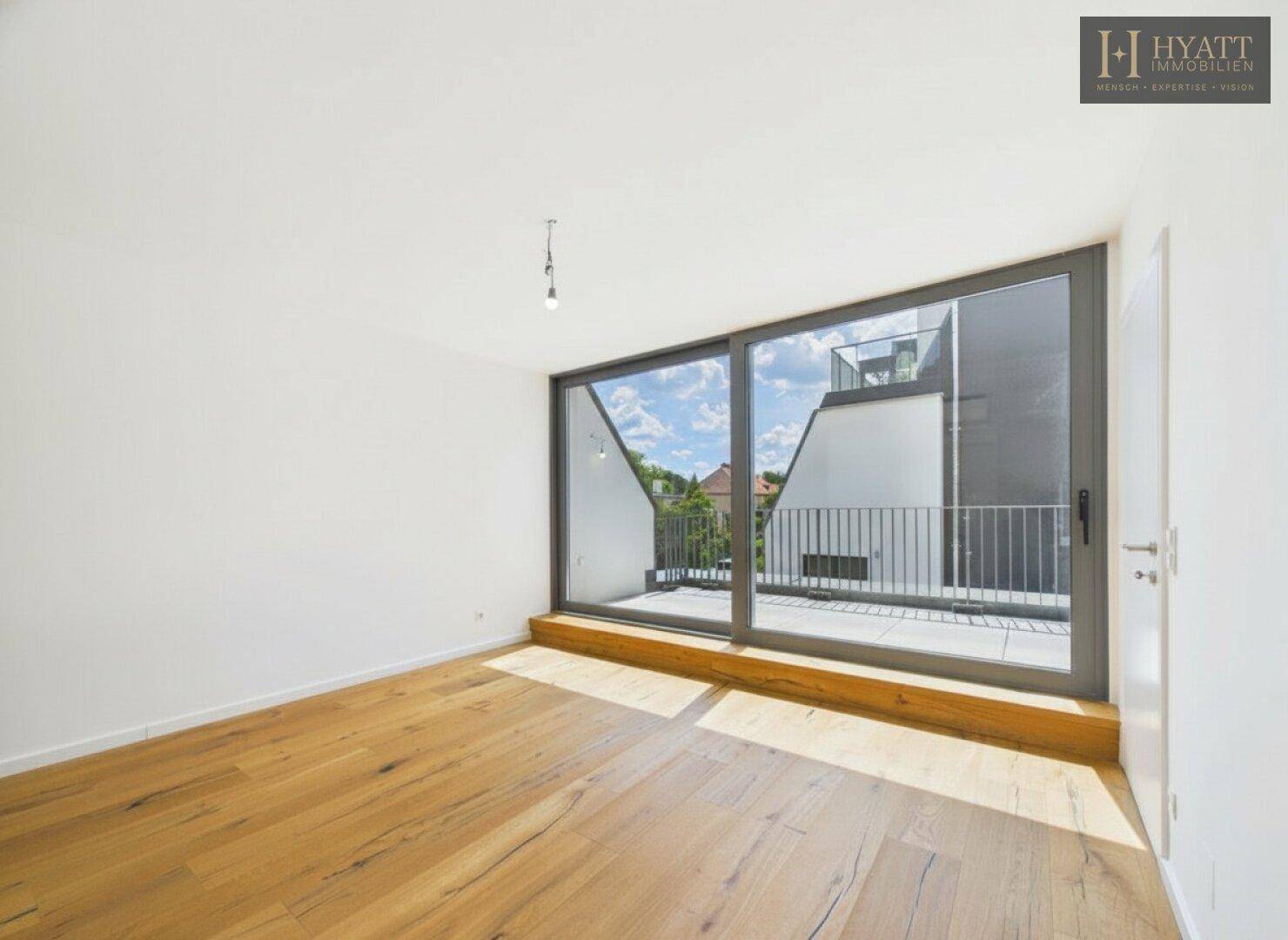 Geräumiges Zimmer mit Holzboden und großer Schiebetür zum Balkon, bietet viel Licht.