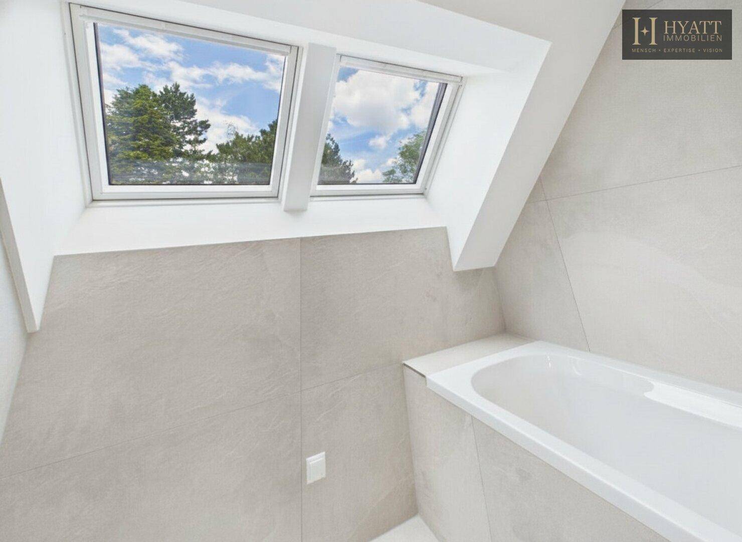 Modernes Badezimmer im Dachgeschoss mit Badewanne, hellen Fliesen und Dachfenstern.