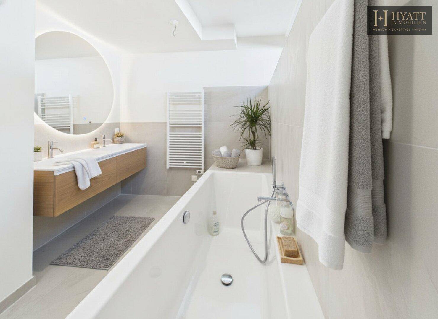 Modernes Badezimmer mit Badewanne, schwebendem Waschtisch und beleuchtetem Rundspiegel.