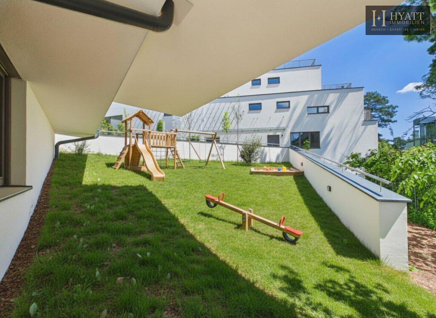 Grüner Gartenbereich mit Spielplatz, Rutsche und Wippe für Kinder.