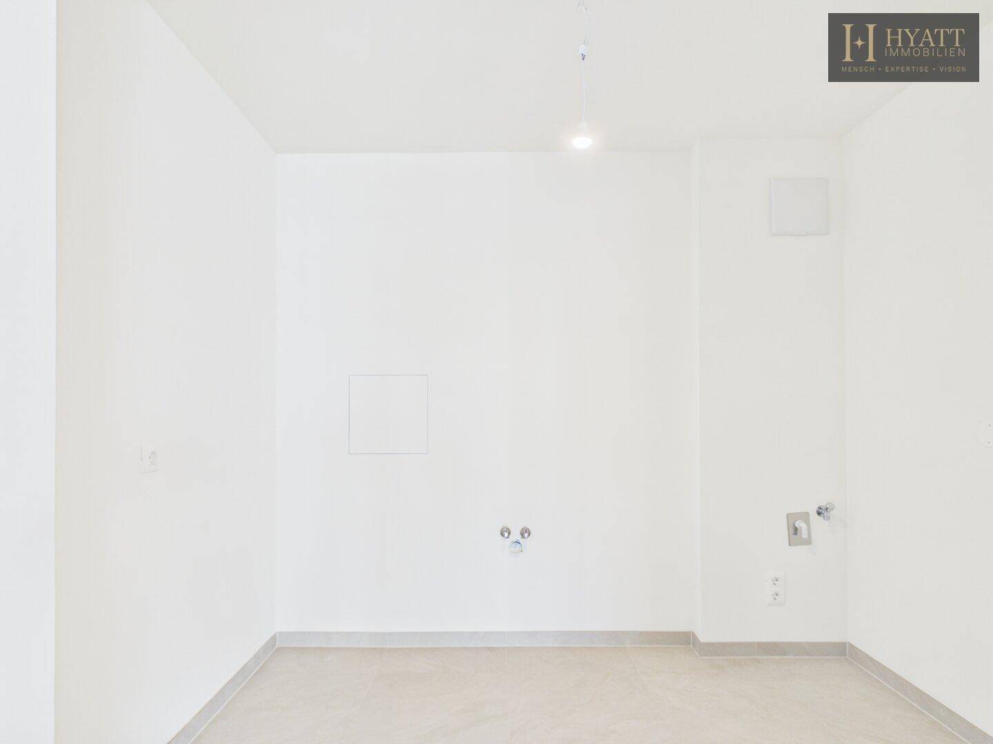 Heller Hauswirtschaftsraum mit Fliesenboden und Anschlüssen für Waschmaschine und Trockner.