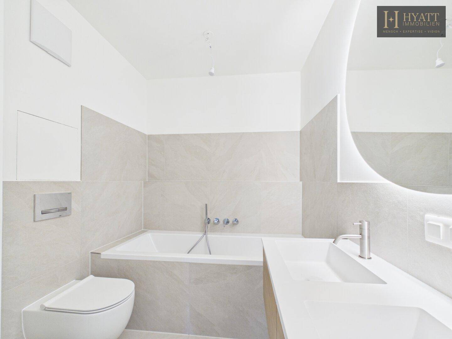 Modernes Badezimmer mit Badewanne, wandhängendem WC und beleuchtetem Spiegel.