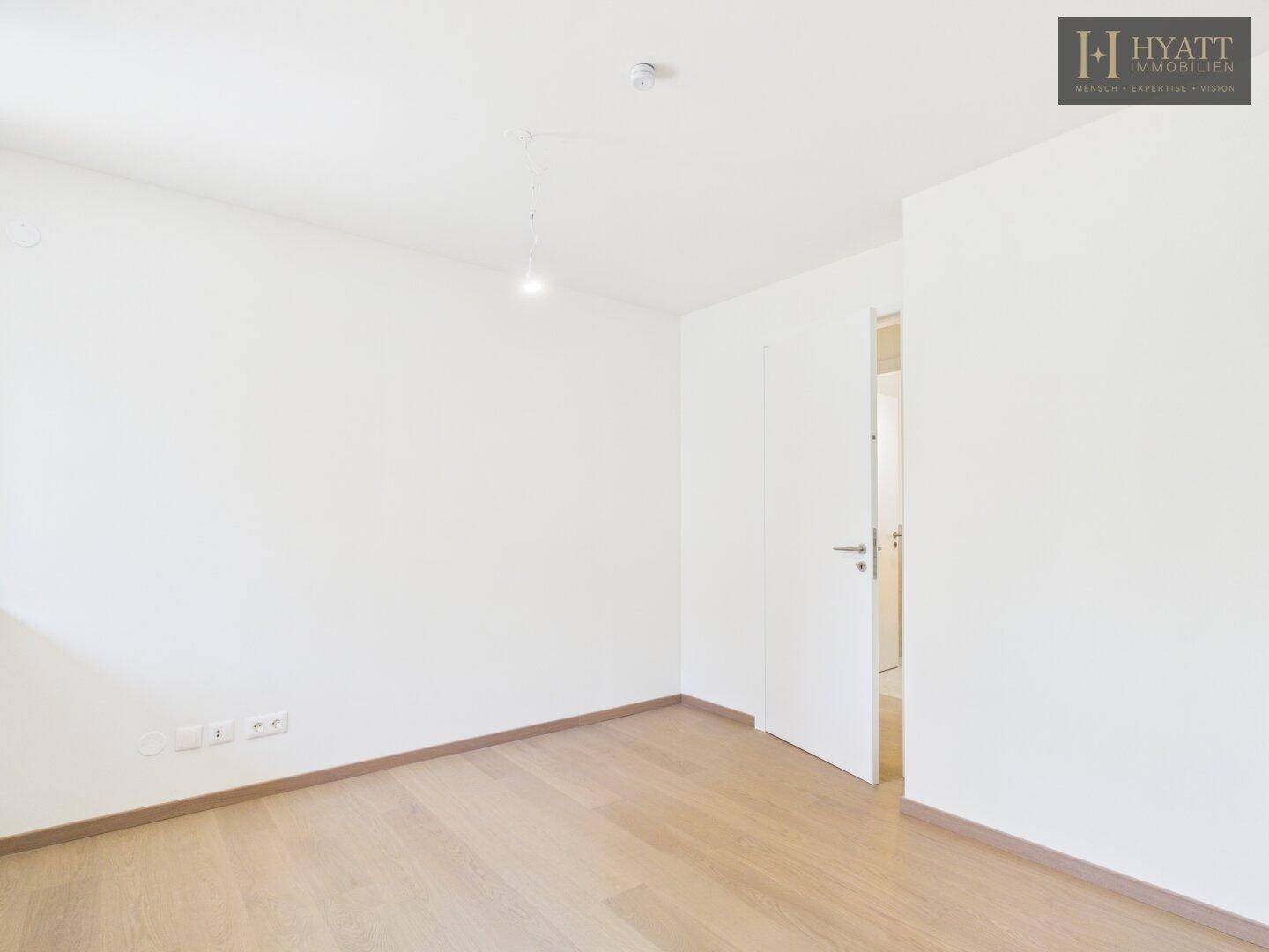 Unmöbliertes Schlafzimmer mit hellem Holzboden und einer modernen weißen Tür.