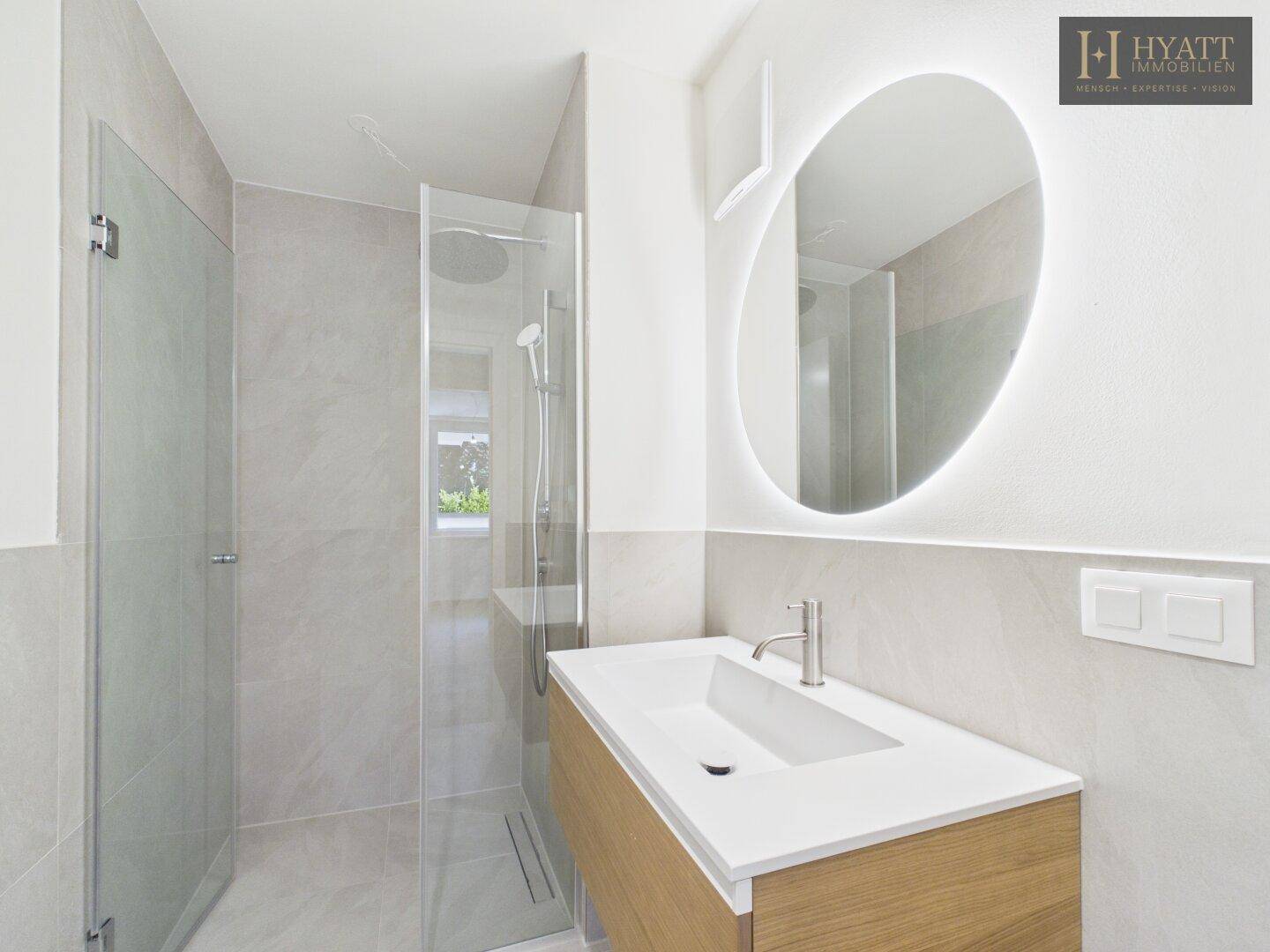 Modernes Badezimmer mit ebenerdiger Dusche, Waschtisch und beleuchtetem Spiegel.