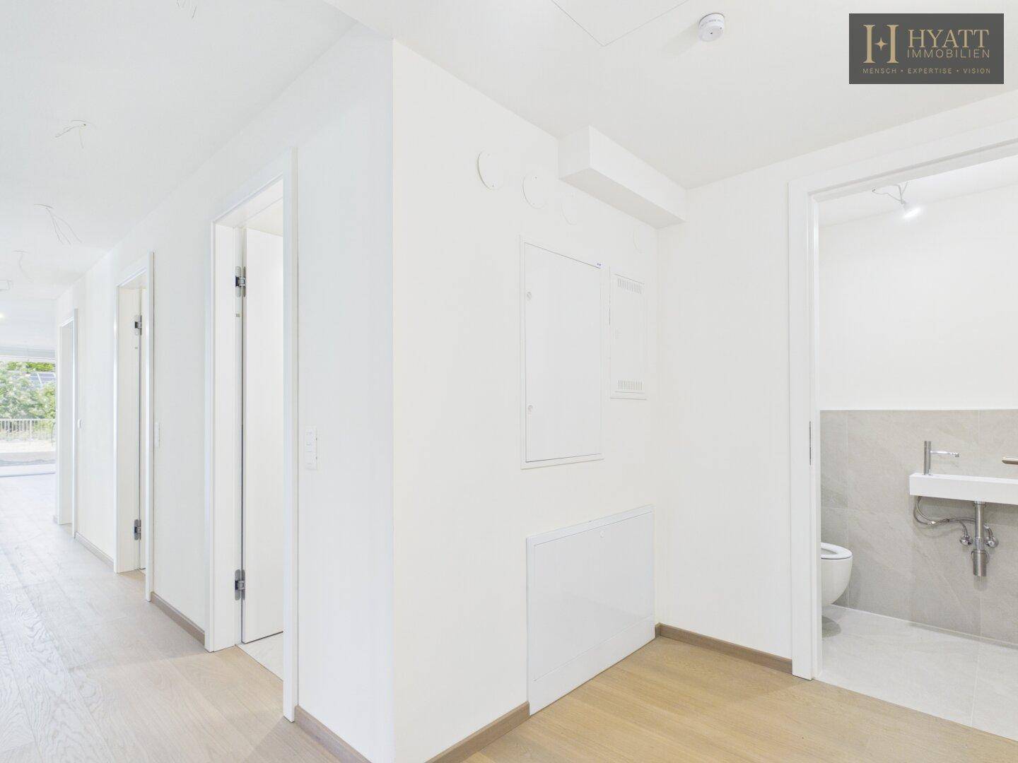 Heller Flur mit Holzboden und Zugang zu einem Gäste-WC und weiteren Räumen.