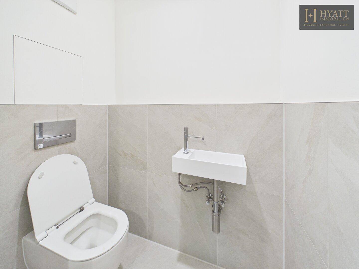 Modernes Gäste-WC mit wandhängender Toilette und kleinem Handwaschbecken.