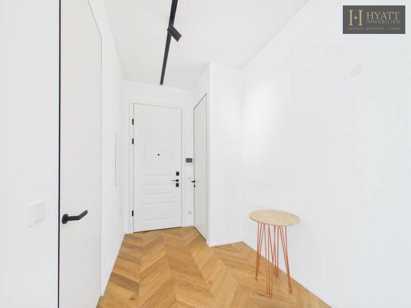 Heller Eingangsbereich mit Fischgrätparkett und moderner weißer Tür, minimalistisch gestaltet.