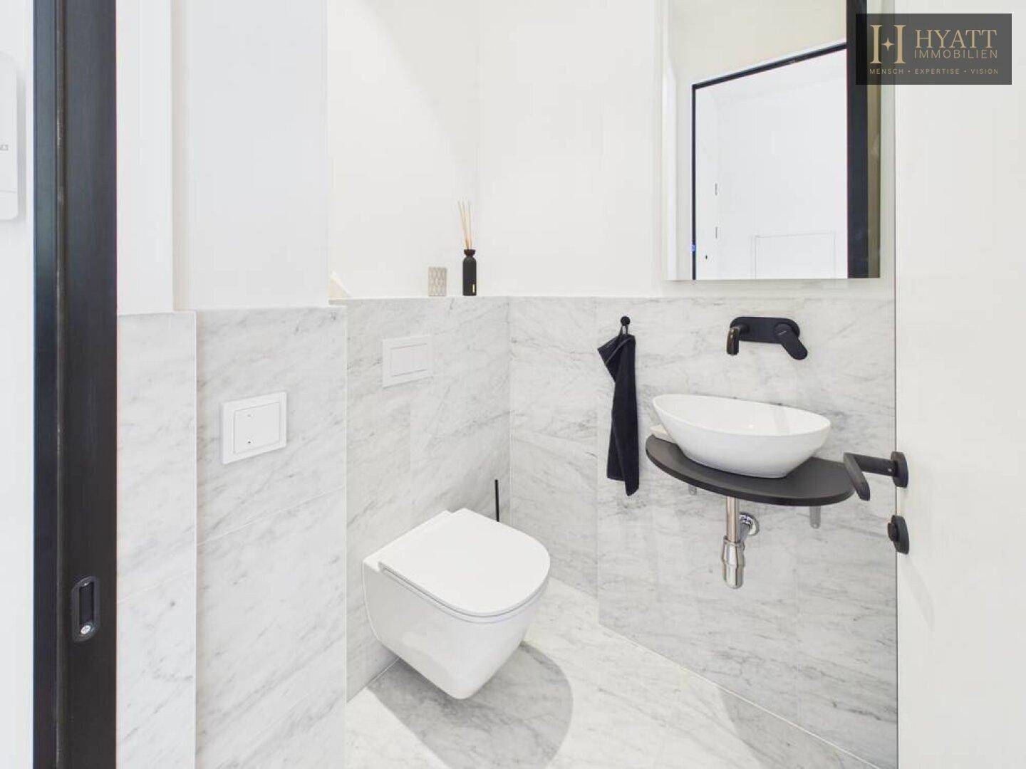 Modernes Gäste-WC mit Marmorfliesen, wandhängendem WC und stilvollem Aufsatzwaschbecken.