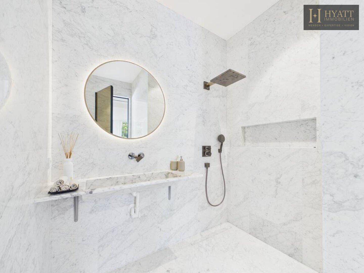 Elegantes Badezimmer mit Marmorfliesen, beleuchtetem Spiegel und einer modernen begehbaren Regendusche.