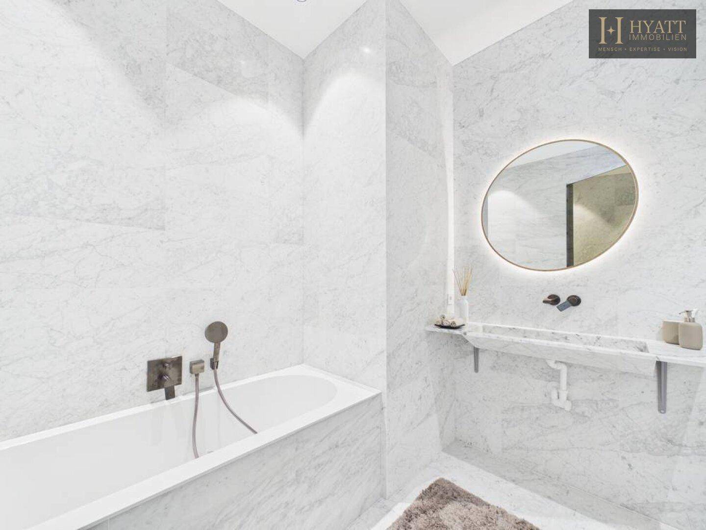 Stilvolles Badezimmer mit Marmorfliesen, Badewanne und modernem Waschtisch mit rundem Spiegel.