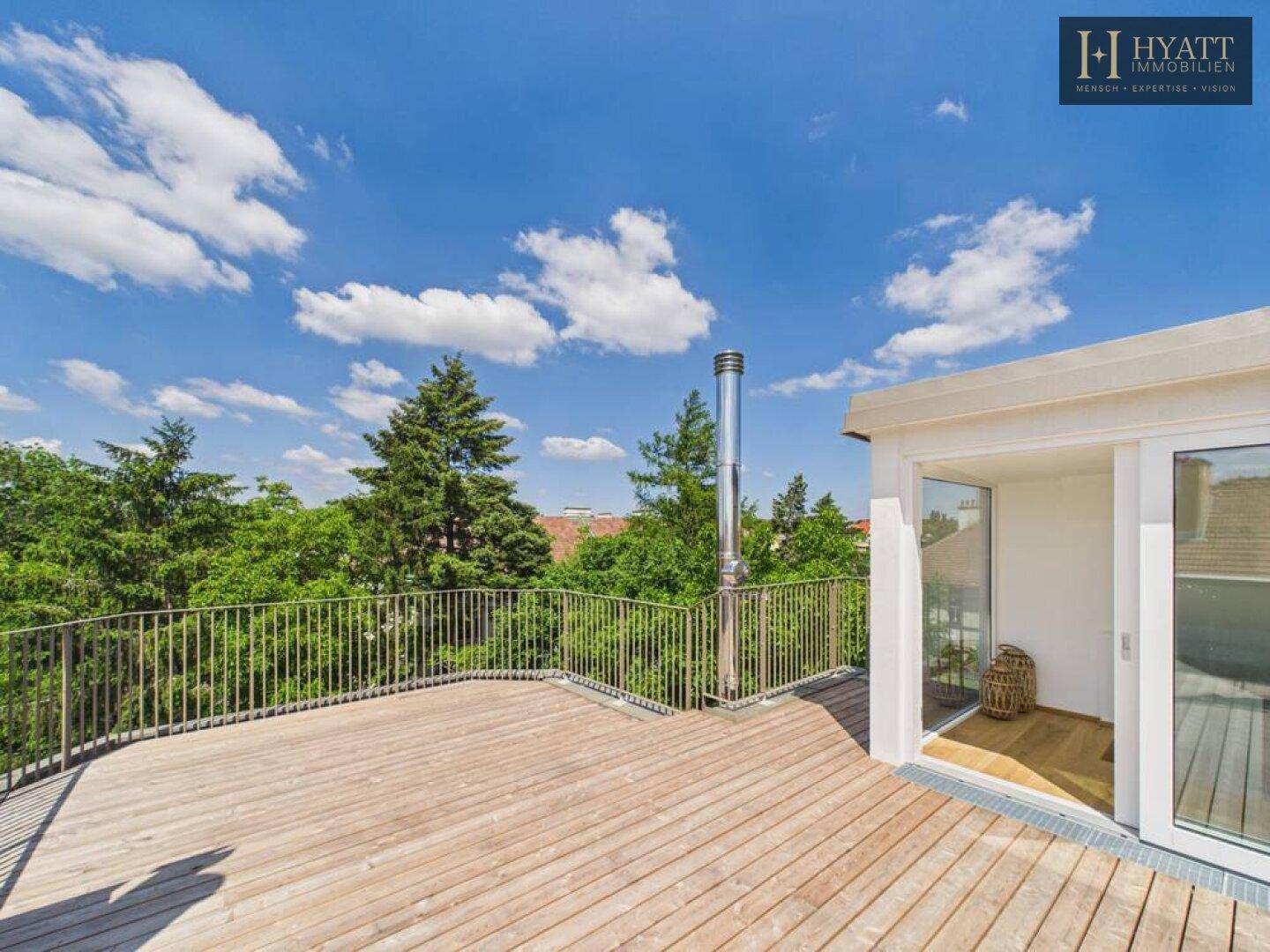 Geräumige Dachterrasse mit Holzboden und Metallgeländer, umgeben von Bäumen und weitem Blick.