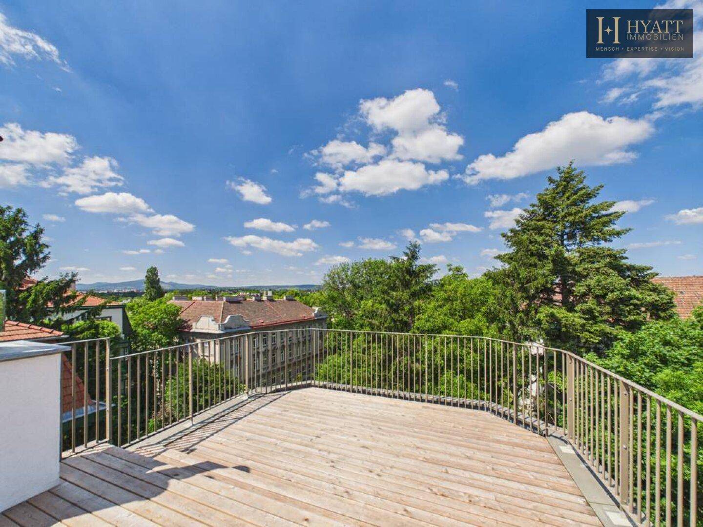 Weitläufige Dachterrasse mit Holzboden, Metallgeländer und Panoramablick über die Stadt und Umgebung.