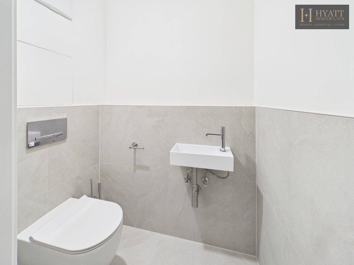 Modernes Gäste-WC mit hellgrauen Fliesen, wandhängendem WC und kleinem Waschbecken.