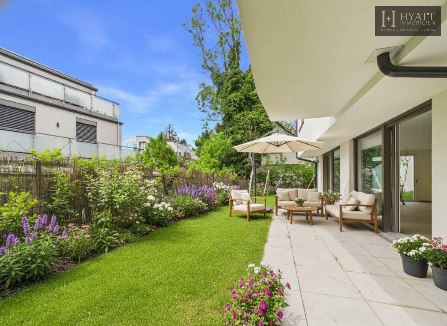 Sonniger Gartenbereich mit Rasenfläche, Blumenbeeten und einer möblierten Terrasse für entspannte Stunden.