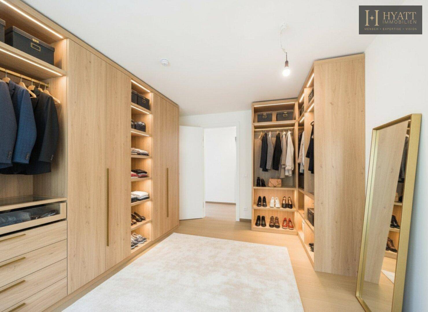 Geräumiger begehbarer Kleiderschrank mit maßgefertigten Holzschränken und integrierter Beleuchtung.