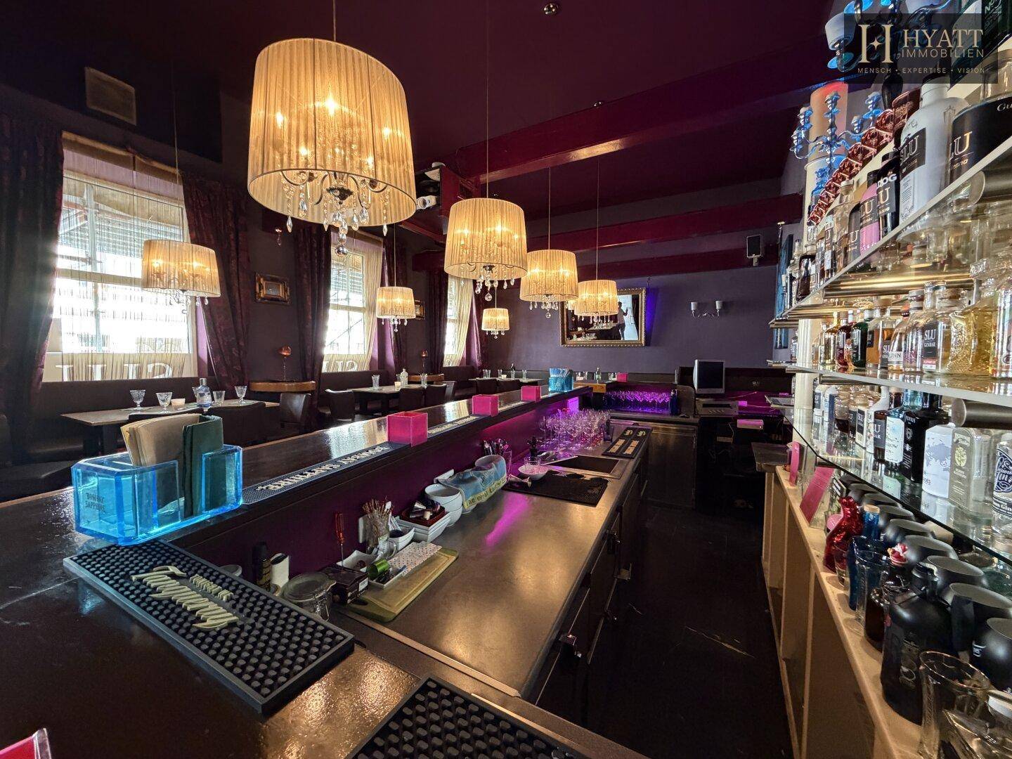 Detailansicht der Bar mit beleuchteter Theke, Flaschenregalen und eleganten Hängelampen.