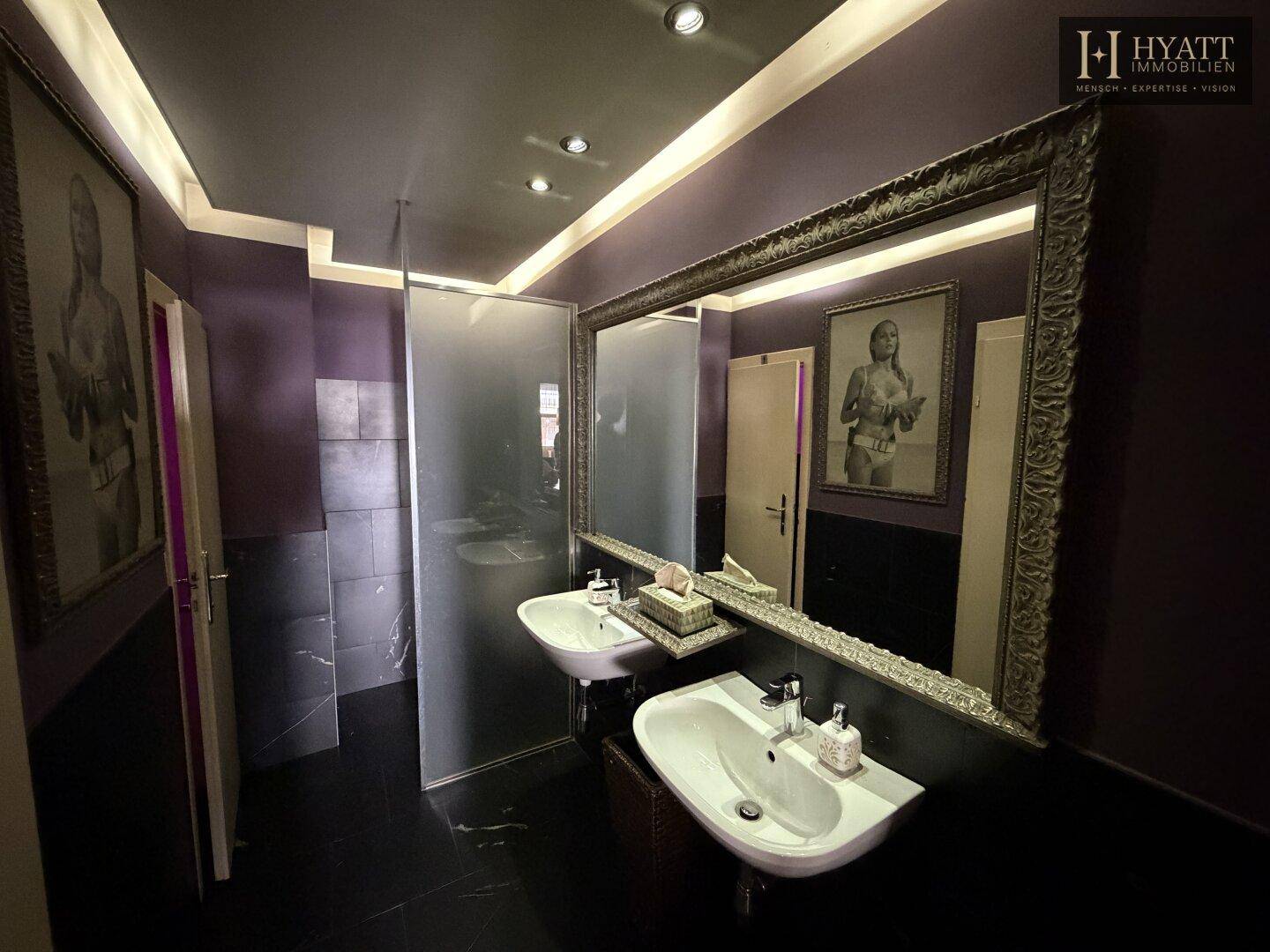Modernes Badezimmer mit zwei Waschbecken, großem Spiegel und dunklen Fliesen an Wänden und Boden.