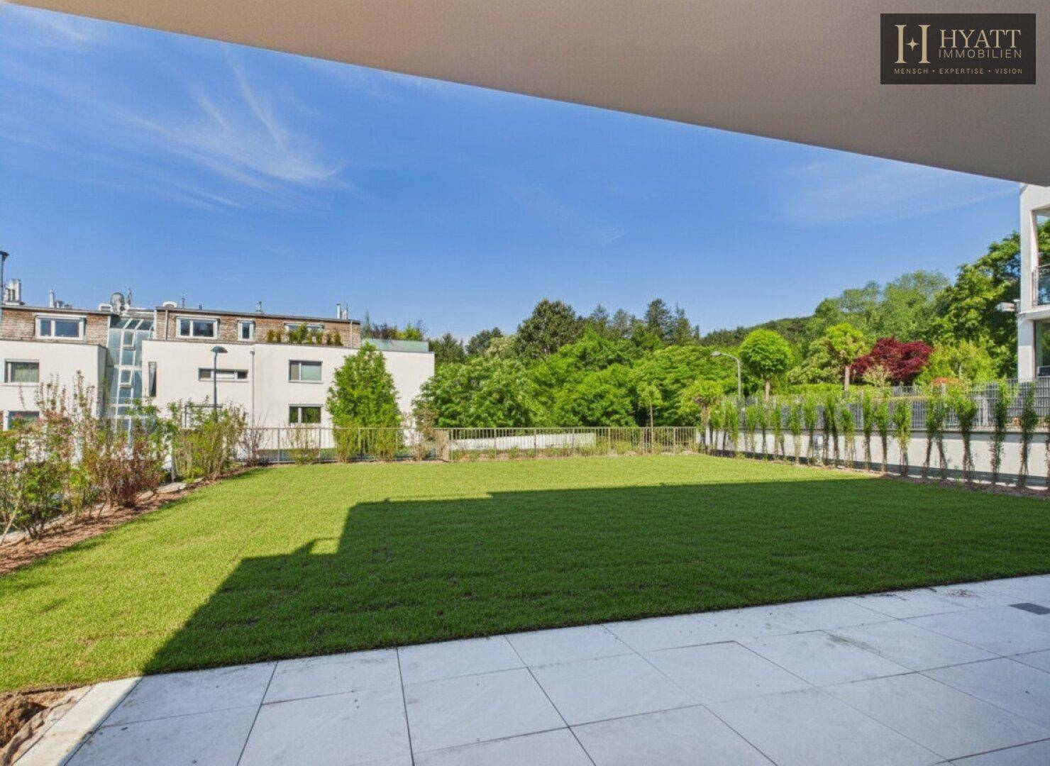 Weitläufige Rasenfläche mit gepflegtem Garten und Blick auf die umliegende Natur.