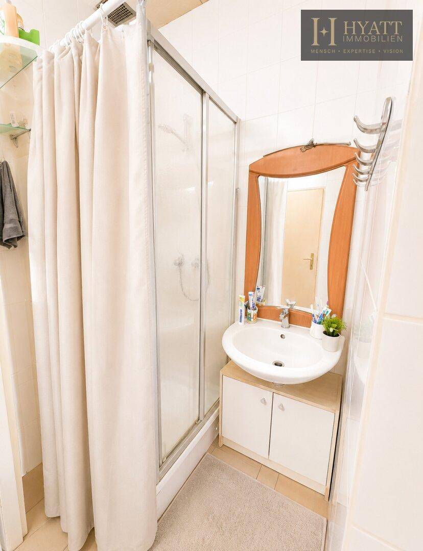 Kleines Badezimmer mit Duschkabine, Waschbecken mit Unterschrank und Wandspiegel.