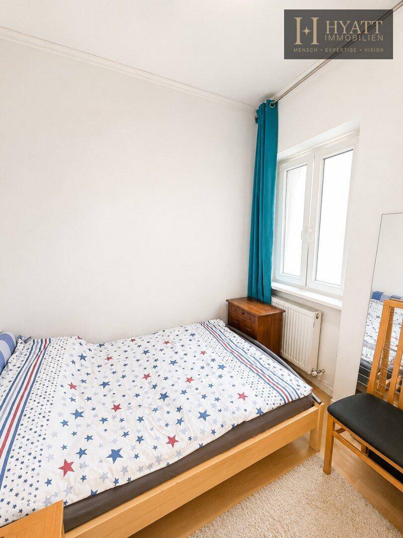 Gemütliches Schlafzimmer mit Einzelbett, Teppichboden und einem Fenster mit blauem Vorhang.
