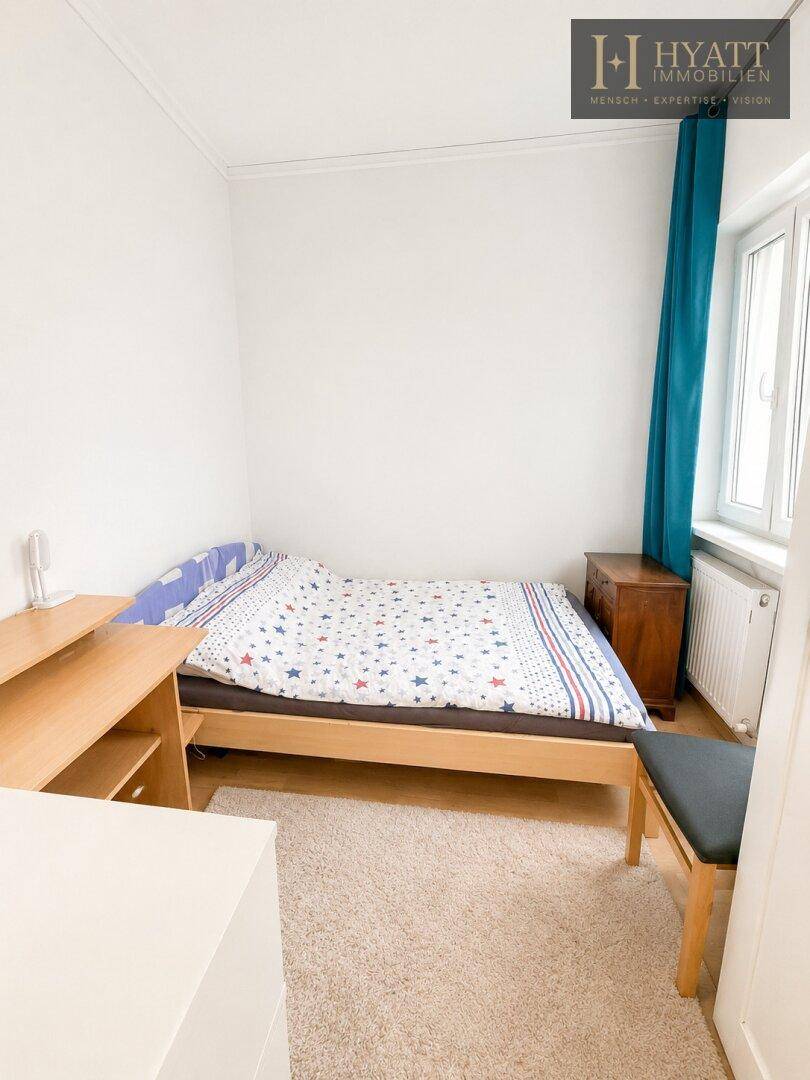 Helles Schlafzimmer mit Einzelbett, Schreibtisch und Teppichboden, ideal als Kinder- oder Gästezimmer.