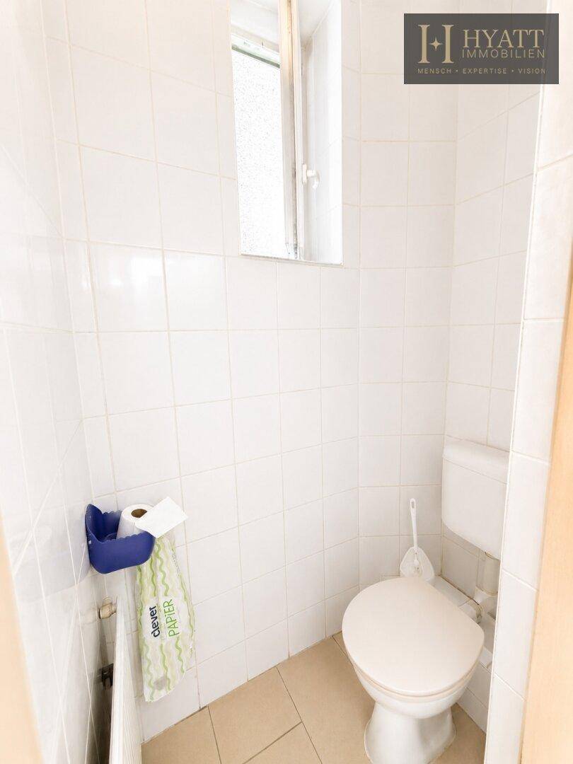 Separates WC mit weißer Toilette, gefliesten Wänden und einem kleinen Fenster für Belüftung.