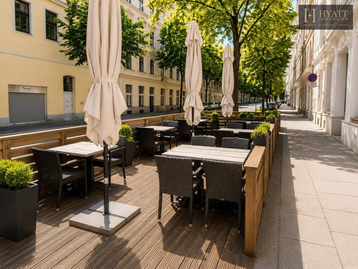 Gemütliche Außenterrasse mit Holzboden, Sonnenschirmen und Rattanmöbeln in urbaner Umgebung.