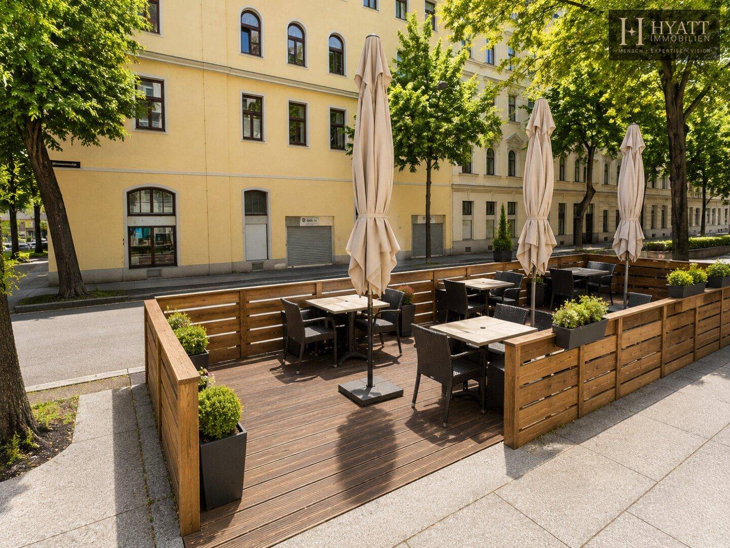 Weitläufige Außenterrasse mit Holzboden, Sonnenschirmen und Blick auf die Stadtstraße.