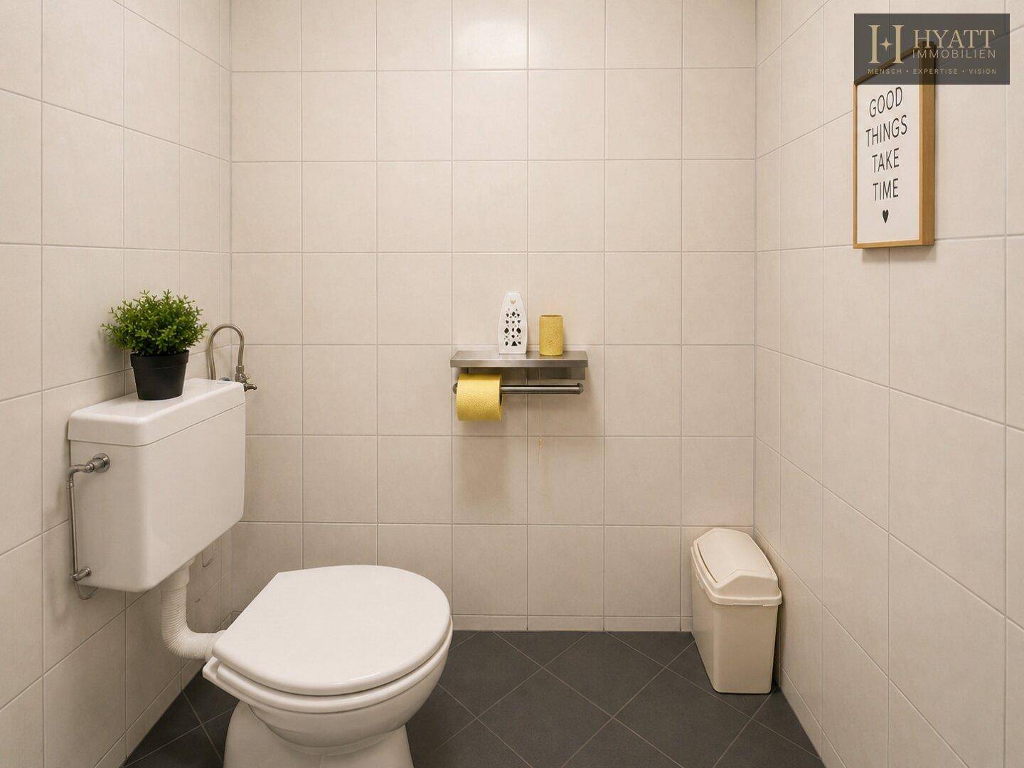 Sauberes WC mit weißen Fliesen, dunklem Boden und einfacher, funktionaler Ausstattung.