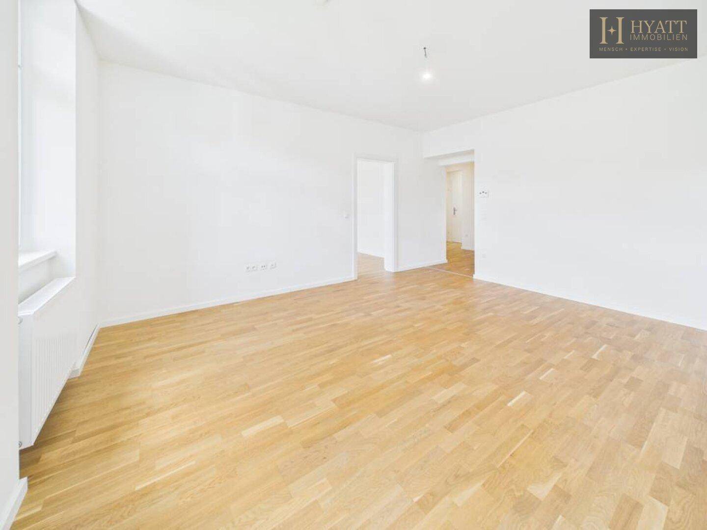 Geräumiges, helles Zimmer mit Parkettboden und offenem Zugang zu weiteren Wohnbereichen.