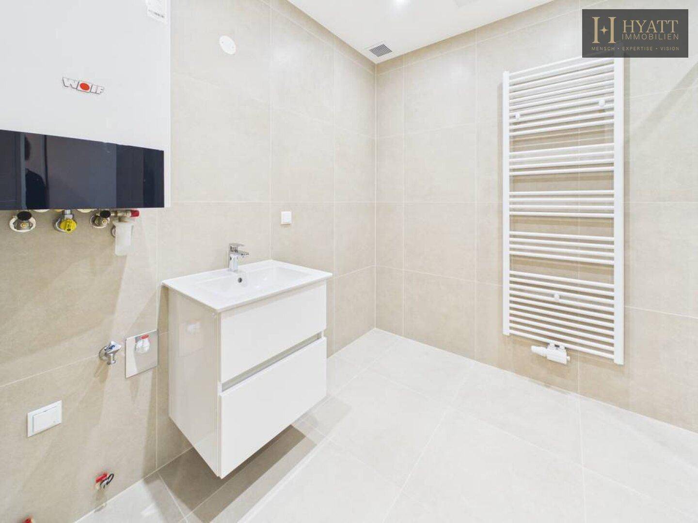 Modernes Badezimmer mit beigefarbenen Fliesen, Waschtischunterschrank und Heiztherme an der Wand.